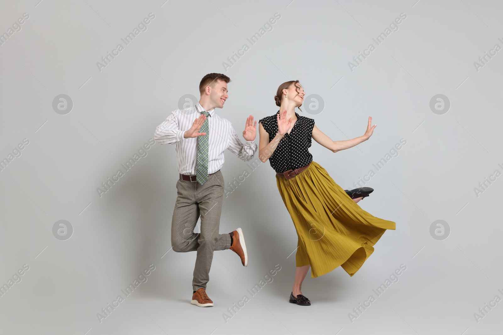 Happy couple in retro outfits dancing on light grey background Photo of Happy couple in retro outfits dancing on light grey background