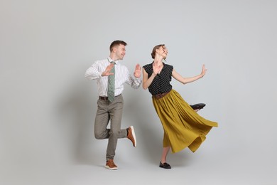 Photo of Happy couple in retro outfits dancing on light grey background
