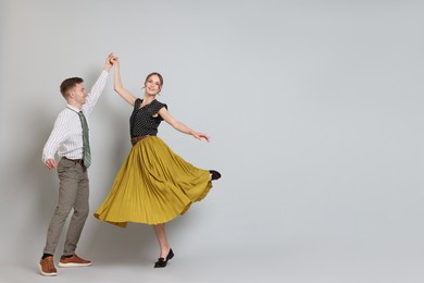 Photo of Happy couple in retro outfits dancing on light grey background, space for text