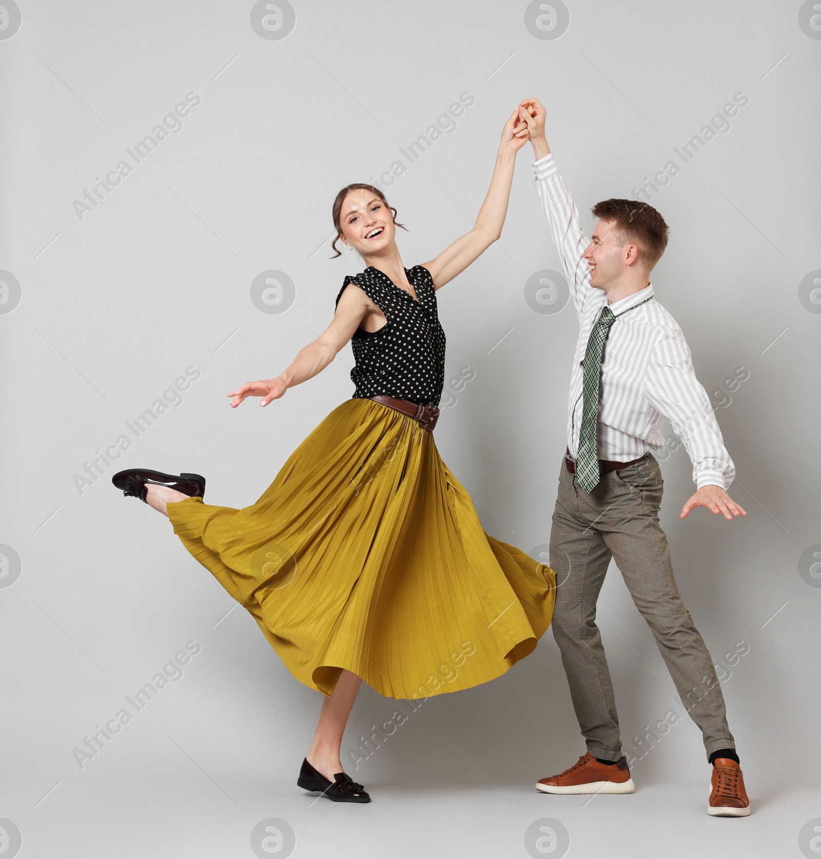 Happy couple in retro outfits dancing on light grey background Photo of Happy couple in retro outfits dancing on light grey background