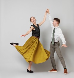 Photo of Happy couple in retro outfits dancing on light grey background