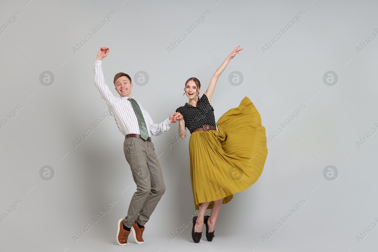 Photo of Happy couple in retro outfits dancing on light grey background