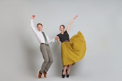 Photo of Happy couple in retro outfits dancing on light grey background
