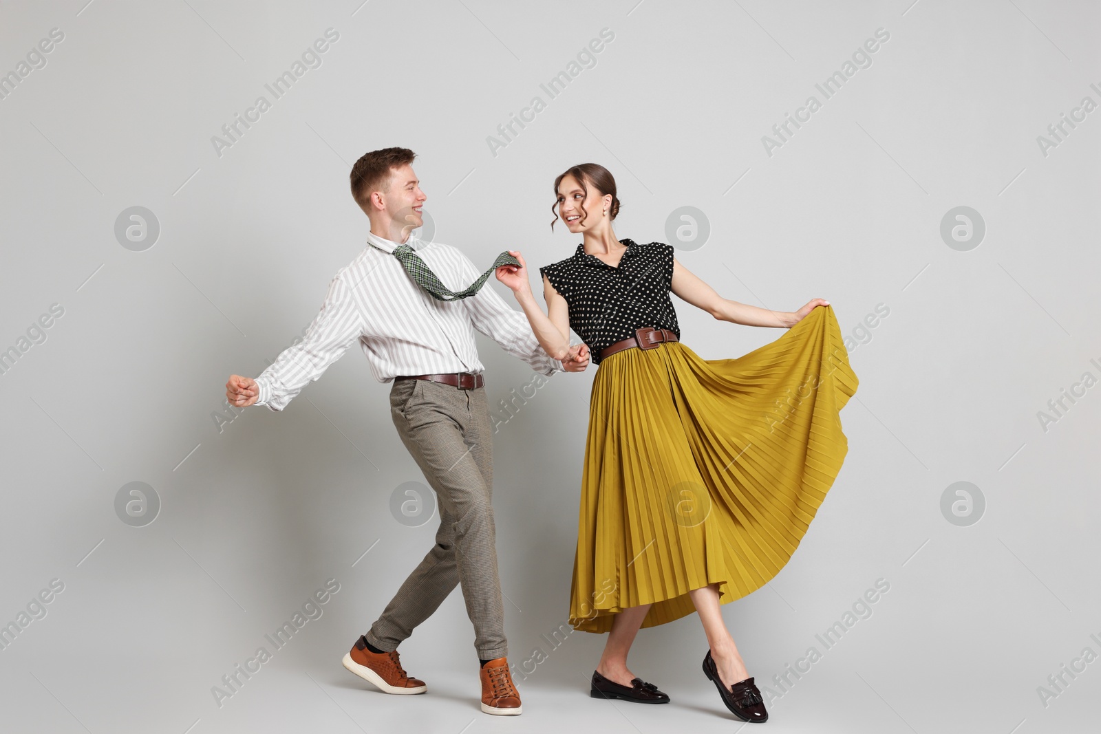 Happy couple in retro outfits dancing on light grey background Photo of Happy couple in retro outfits dancing on light grey background