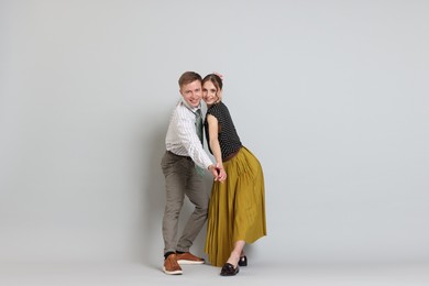 Photo of Happy couple in retro outfits dancing on light grey background