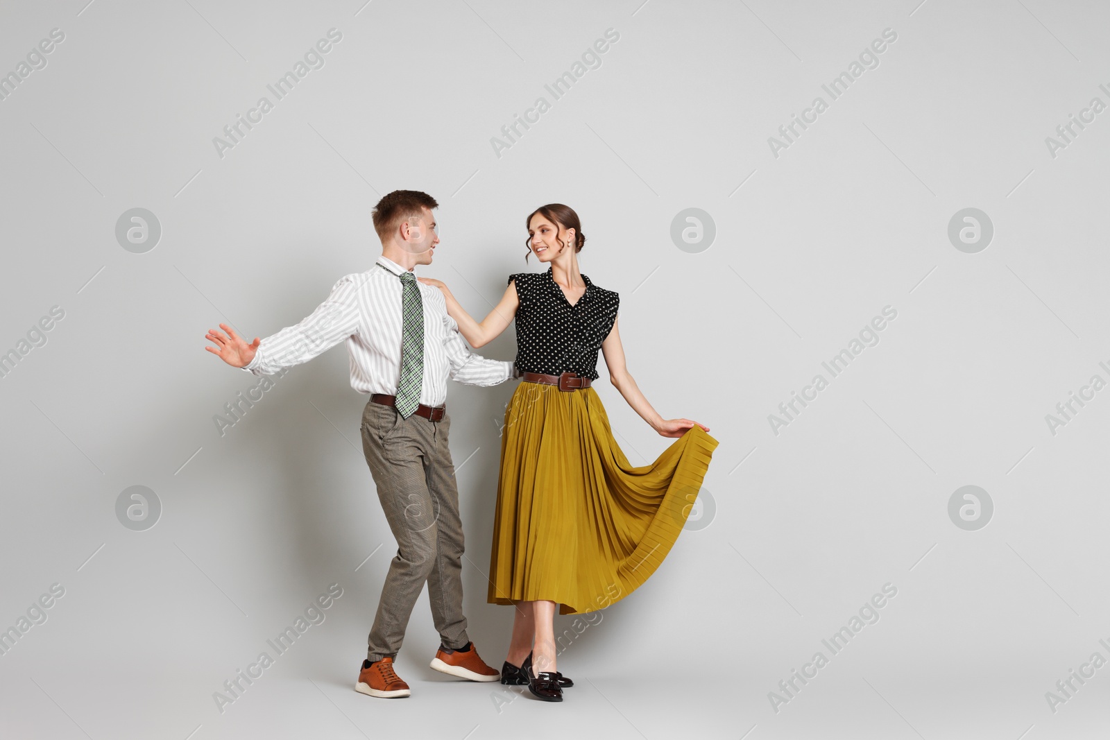 Happy couple in retro outfits dancing on light grey background, space for text Photo of Happy couple in retro outfits dancing on light grey background, space for text