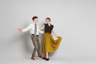 Photo of Happy couple in retro outfits dancing on light grey background, space for text