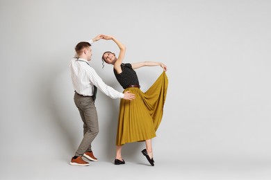 Photo of Happy couple in retro outfits dancing on light grey background, space for text