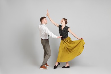 Photo of Happy couple in retro outfits dancing on light grey background