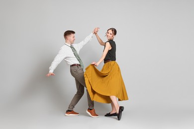 Photo of Happy couple in retro outfits dancing on light grey background