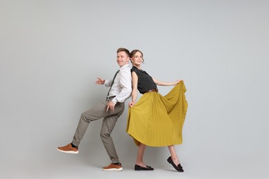 Photo of Happy couple in retro outfits dancing on light grey background