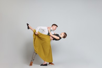 Photo of Happy couple in retro outfits dancing on light grey background, space for text