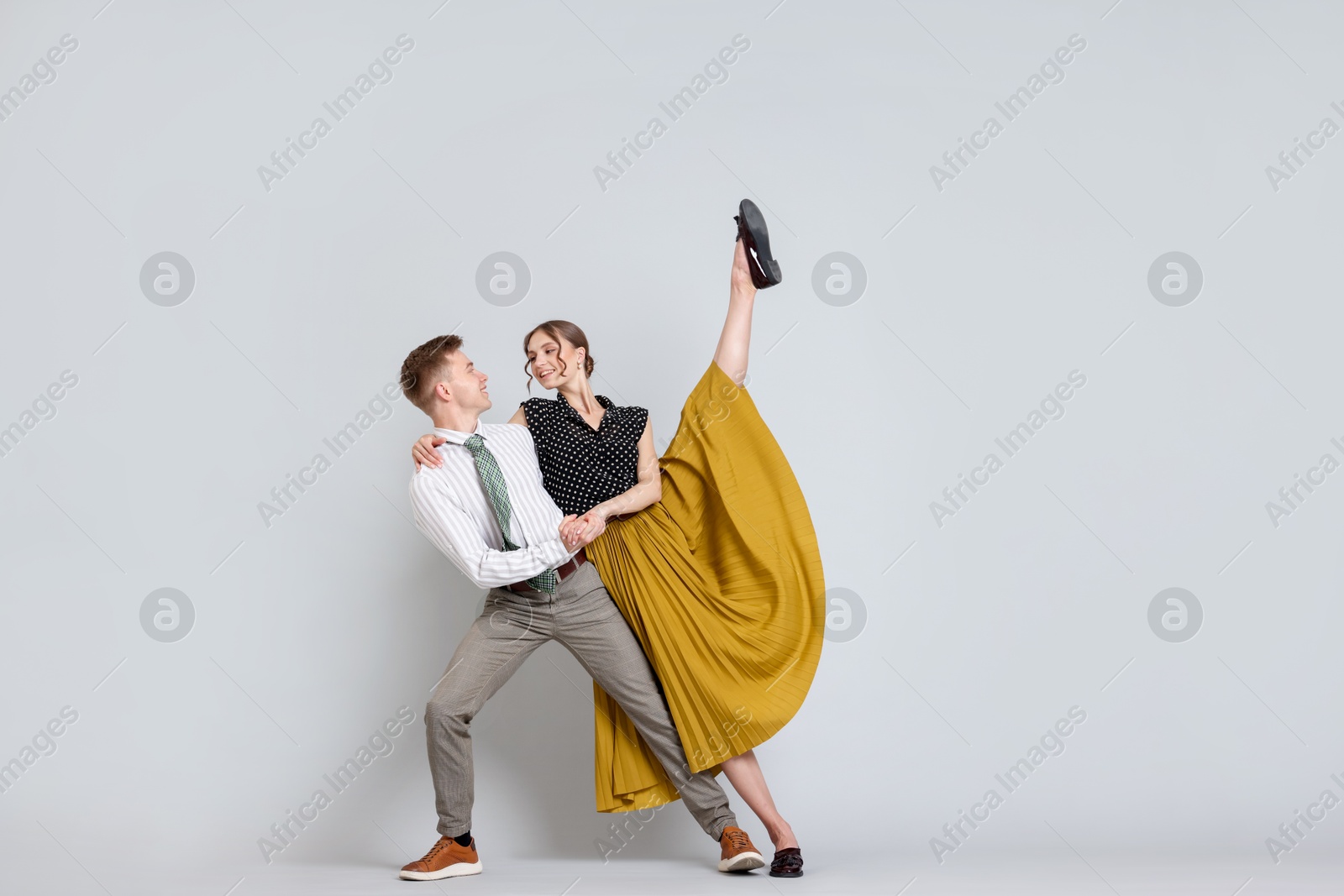 Happy couple in retro outfits dancing on light grey background, space for text Photo of Happy couple in retro outfits dancing on light grey background, space for text