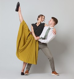 Photo of Happy couple in retro outfits dancing on light grey background