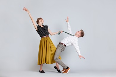 Photo of Happy couple in retro outfits dancing on light grey background