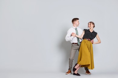Photo of Happy couple in retro outfits dancing on light grey background, space for text