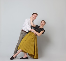 Photo of Happy couple in retro outfits dancing on light grey background