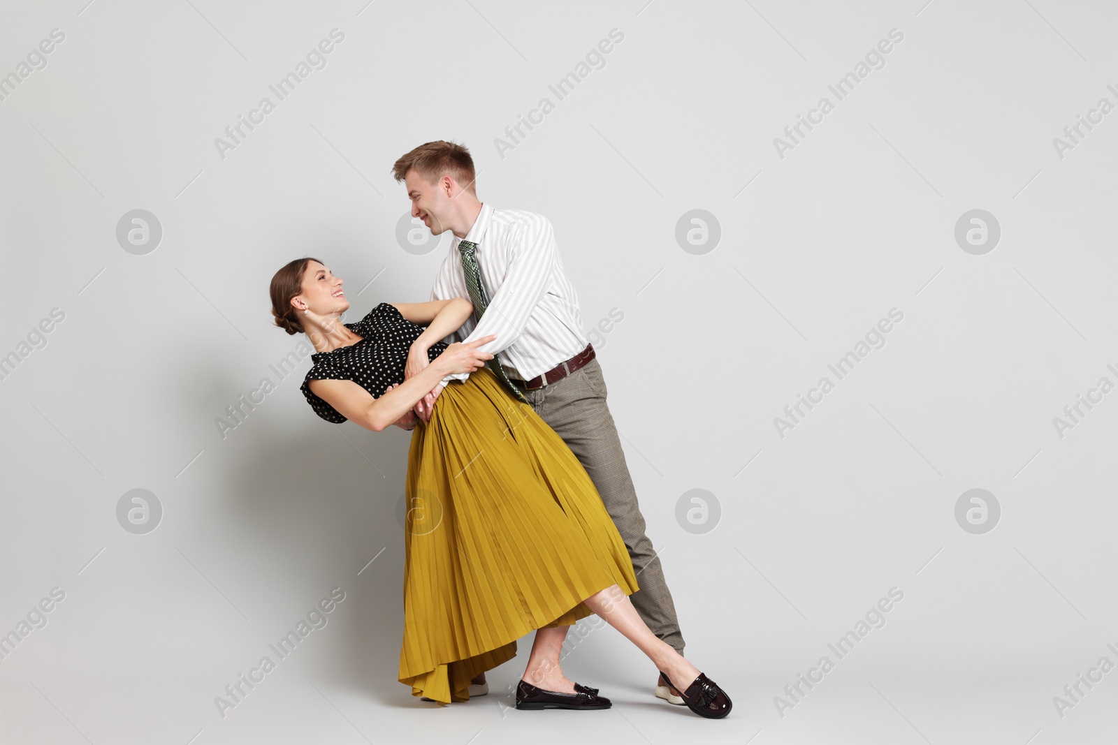 Photo of Happy couple in retro outfits dancing on light grey background, space for text