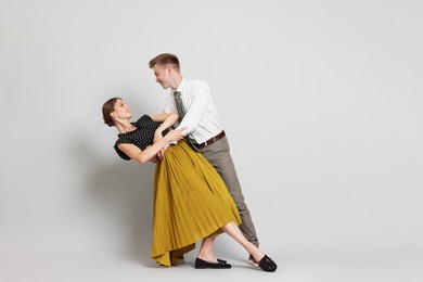 Photo of Happy couple in retro outfits dancing on light grey background, space for text