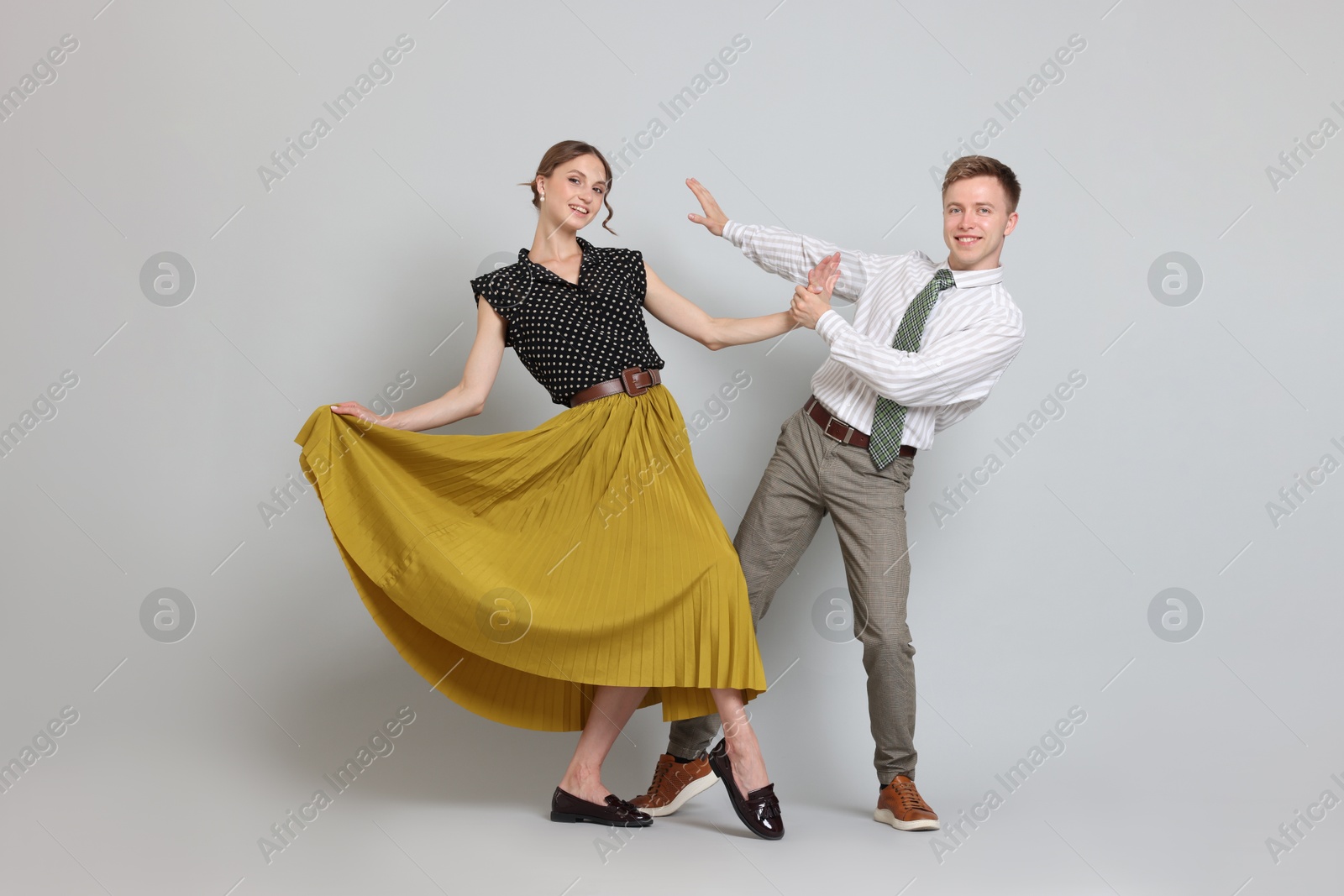 Photo of Happy couple in retro outfits dancing on light grey background