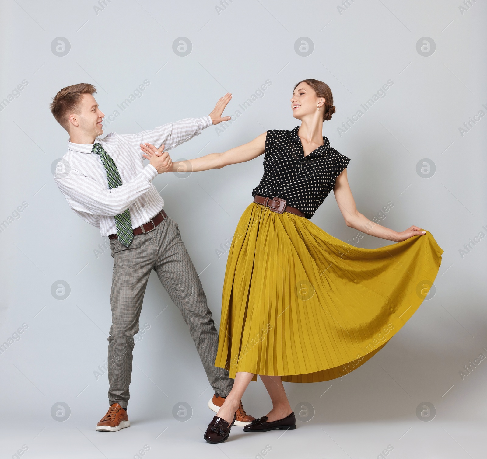 Photo of Happy couple in retro outfits dancing on light grey background