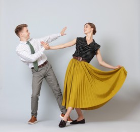 Photo of Happy couple in retro outfits dancing on light grey background