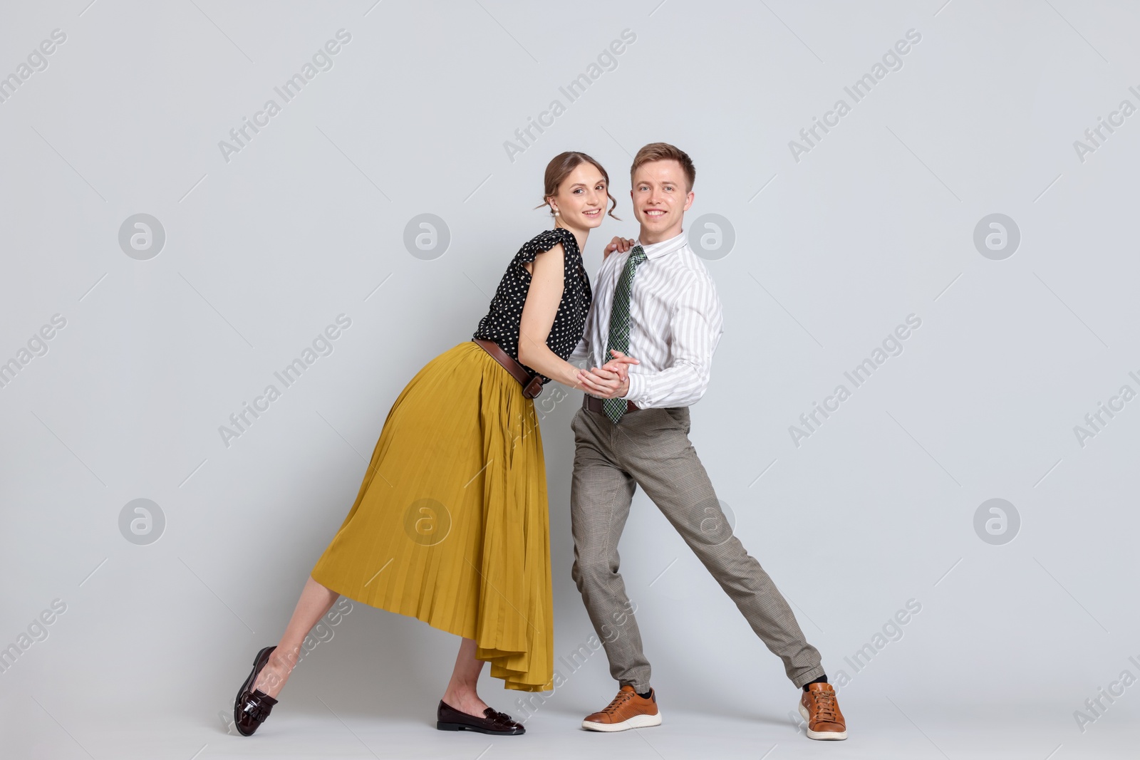 Photo of Happy couple in retro outfits dancing on light grey background