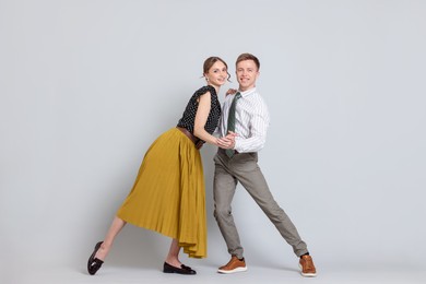 Photo of Happy couple in retro outfits dancing on light grey background