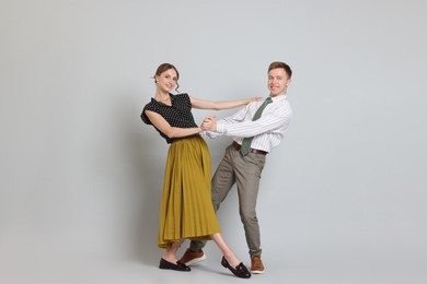 Photo of Happy couple in retro outfits dancing on light grey background