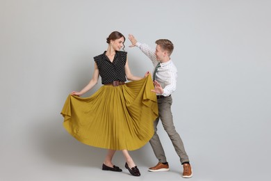 Photo of Happy couple in retro outfits dancing on light grey background