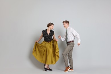 Photo of Happy couple in retro outfits dancing on light grey background