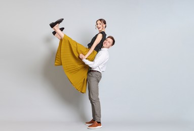 Photo of Happy couple in retro outfits dancing on light grey background
