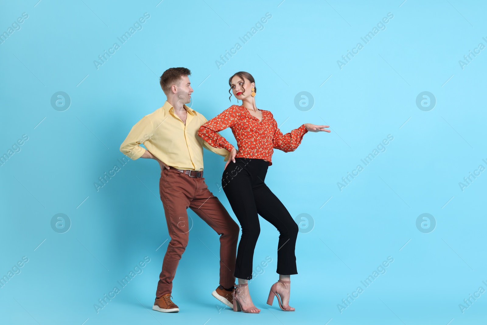 Happy couple in retro outfits dancing on light blue background Photo of Happy couple in retro outfits dancing on light blue background
