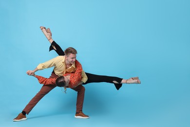 Photo of Happy couple in retro outfits dancing on light blue background, space for text