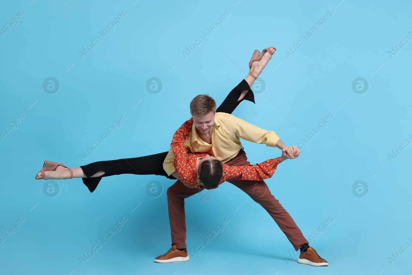 Photo of Happy couple in retro outfits dancing on light blue background