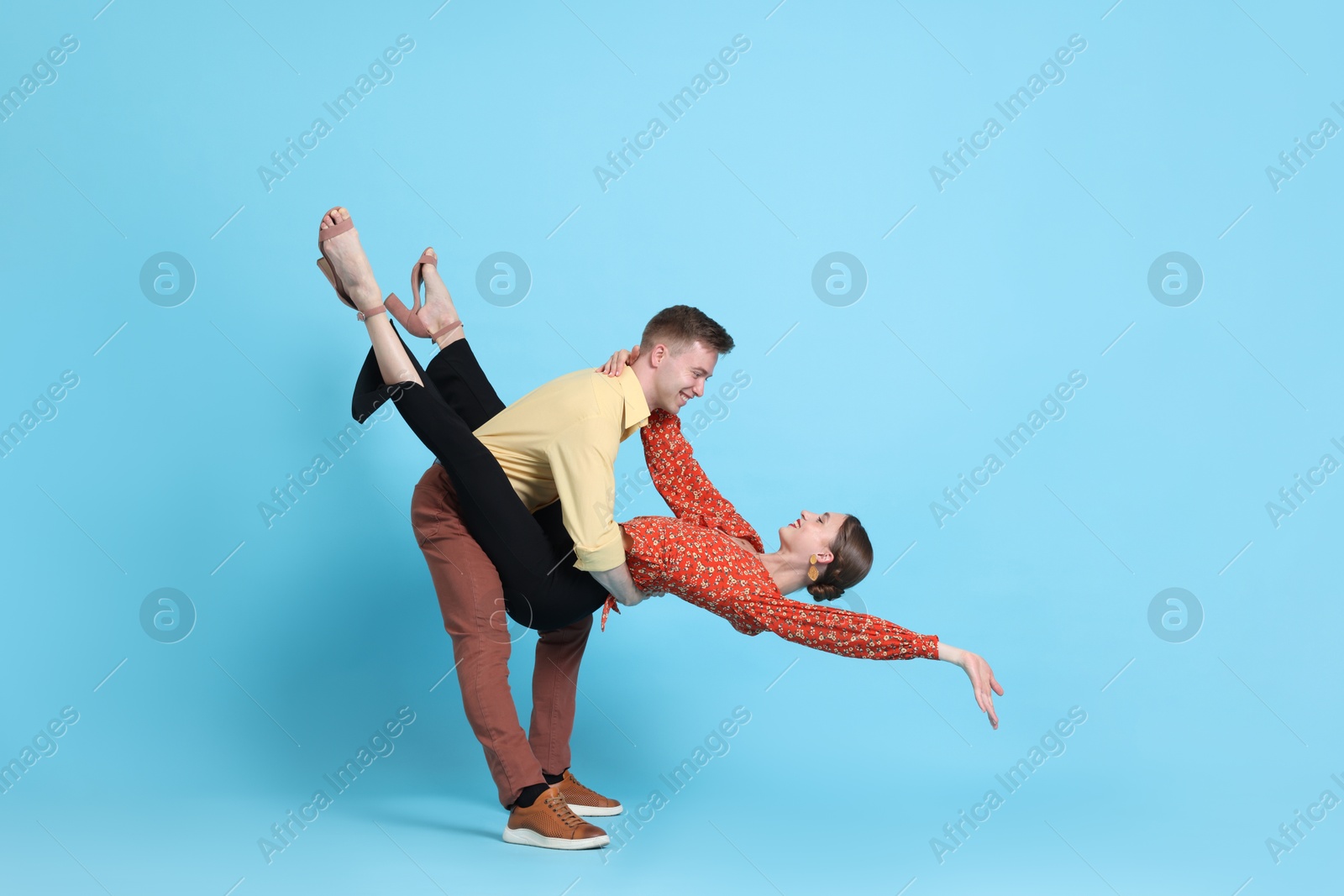 Happy couple in retro outfits dancing on light blue background Photo of Happy couple in retro outfits dancing on light blue background