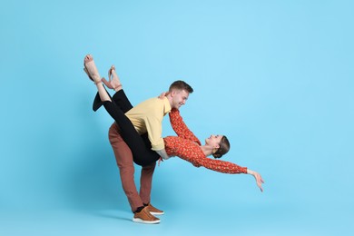 Photo of Happy couple in retro outfits dancing on light blue background