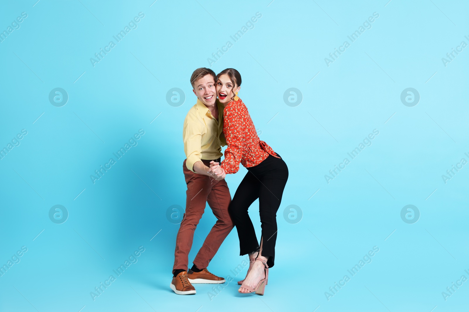 Photo of Happy couple in retro outfits dancing on light blue background