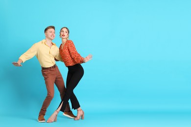 Photo of Happy couple in retro outfits dancing on light blue background, space for text