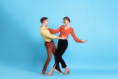 Photo of Happy couple in retro outfits dancing on light blue background