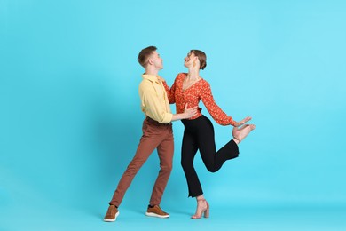 Photo of Happy couple in retro outfits dancing on light blue background