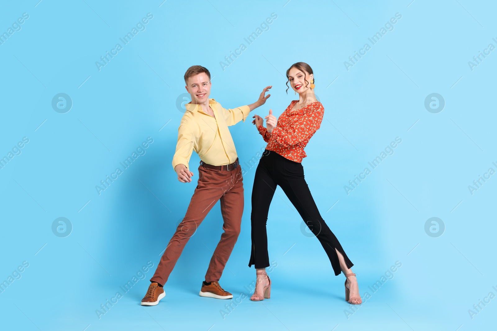 Happy couple in retro outfits dancing on light blue background Photo of Happy couple in retro outfits dancing on light blue background