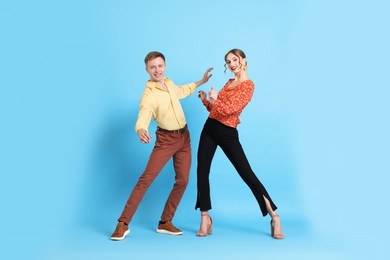 Photo of Happy couple in retro outfits dancing on light blue background