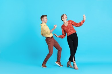 Photo of Happy couple in retro outfits dancing on light blue background