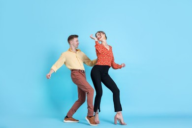Photo of Happy couple in retro outfits dancing on light blue background