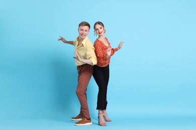 Photo of Happy couple in retro outfits dancing on light blue background
