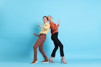 Photo of Happy couple in retro outfits dancing on light blue background