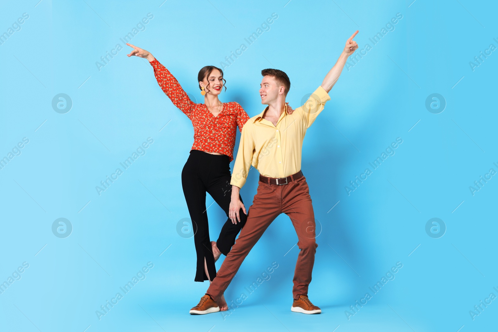 Happy couple in retro outfits dancing on light blue background Photo of Happy couple in retro outfits dancing on light blue background