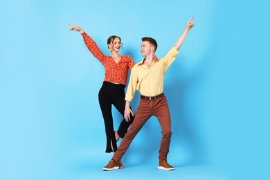 Photo of Happy couple in retro outfits dancing on light blue background