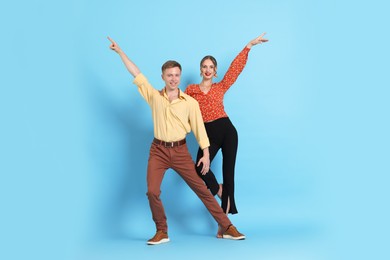 Photo of Happy couple in retro outfits dancing on light blue background